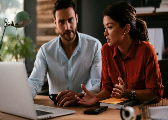 A man and a woman sitting at a desk looking at their computer, potentially researching digital marketing optimization strategies online