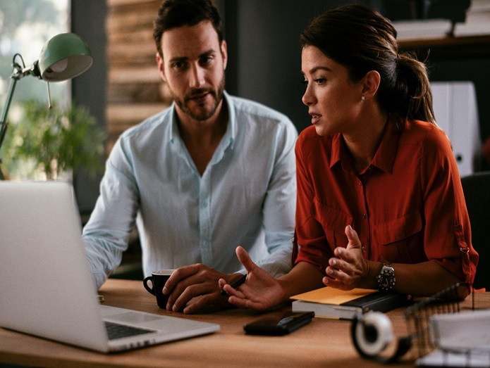 A man and a woman sitting at a desk looking at their computer, potentially researching digital marketing optimization strategies online
